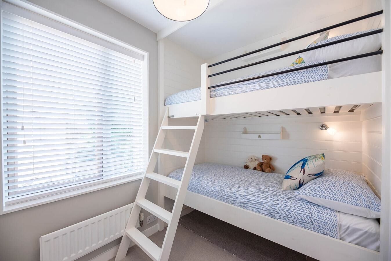 Une chambre avec un lit superposé, une échelle, une fenêtre avec des stores et un radiateur.