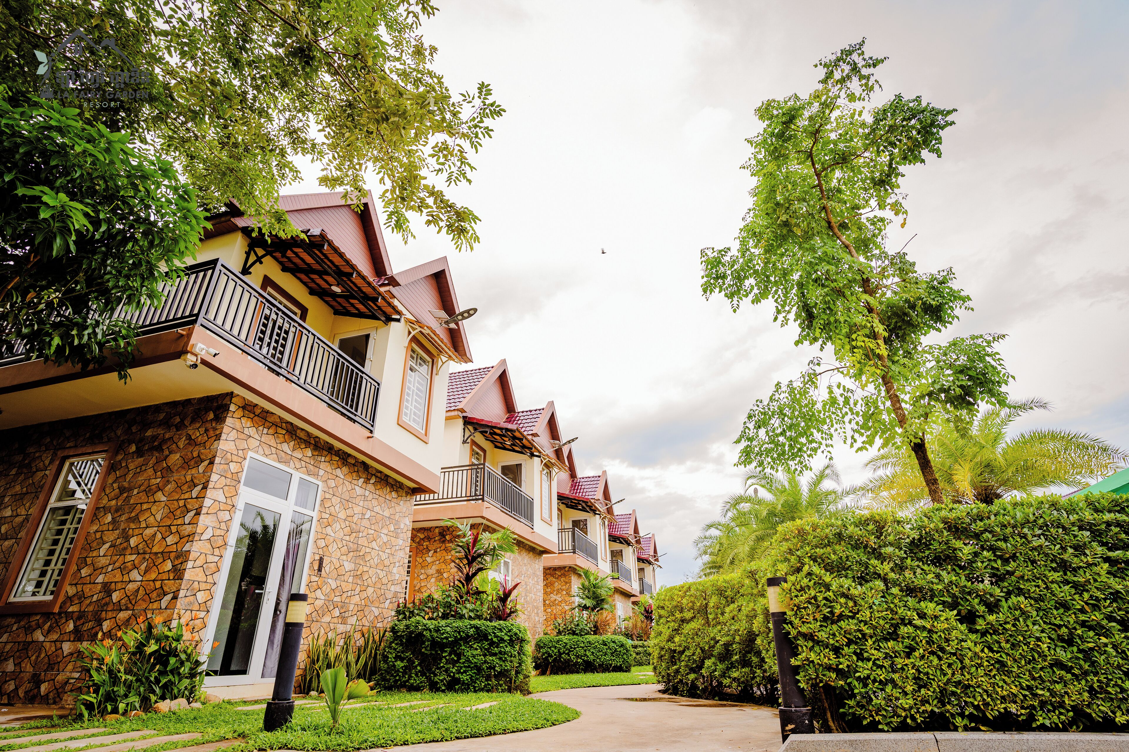 A row of modern, multi-story residential buildings with balconies, surrounded by lush greenery and a well-maintained garden.