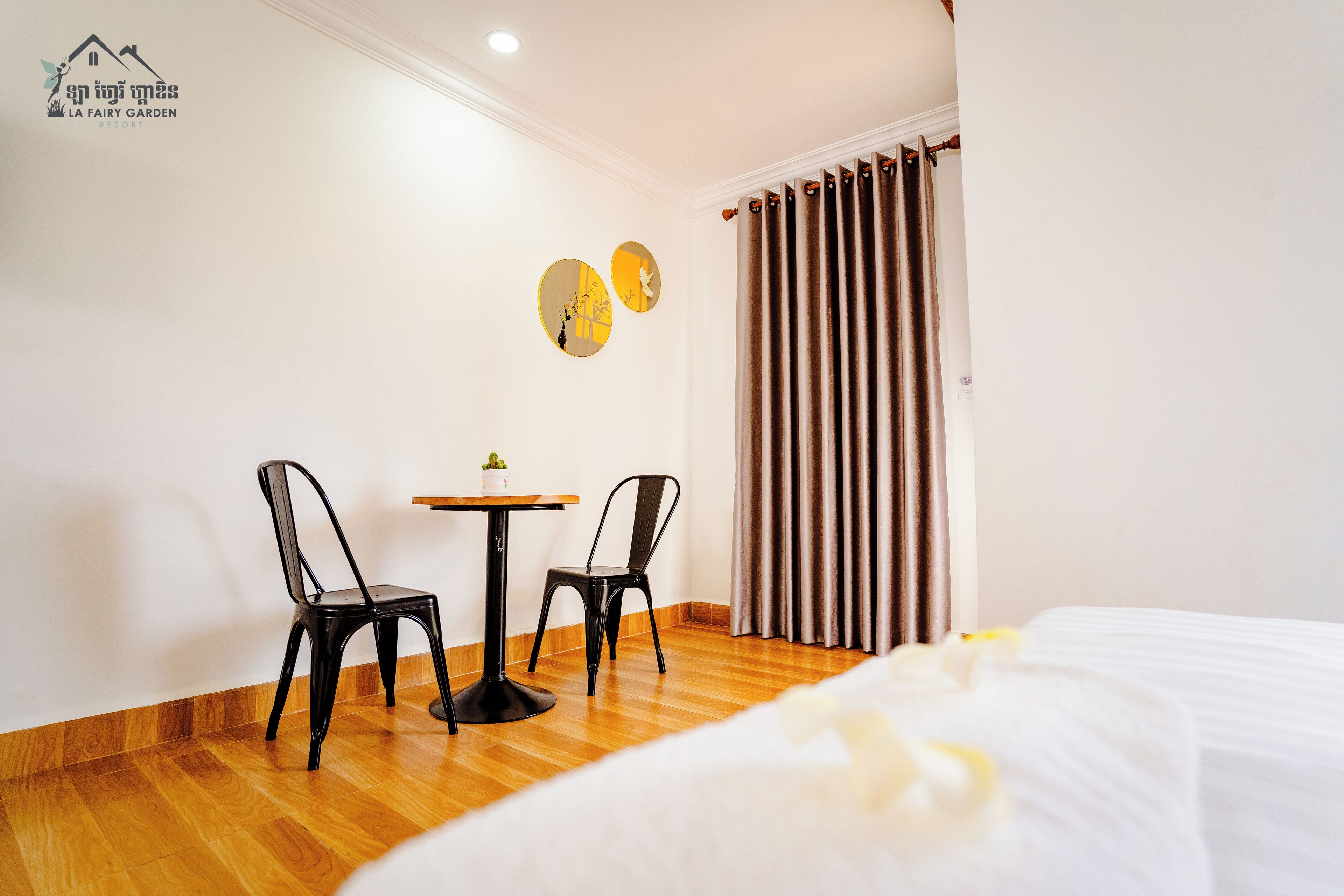 A hotel room with a bed, a small table with chairs, and a window with curtains.