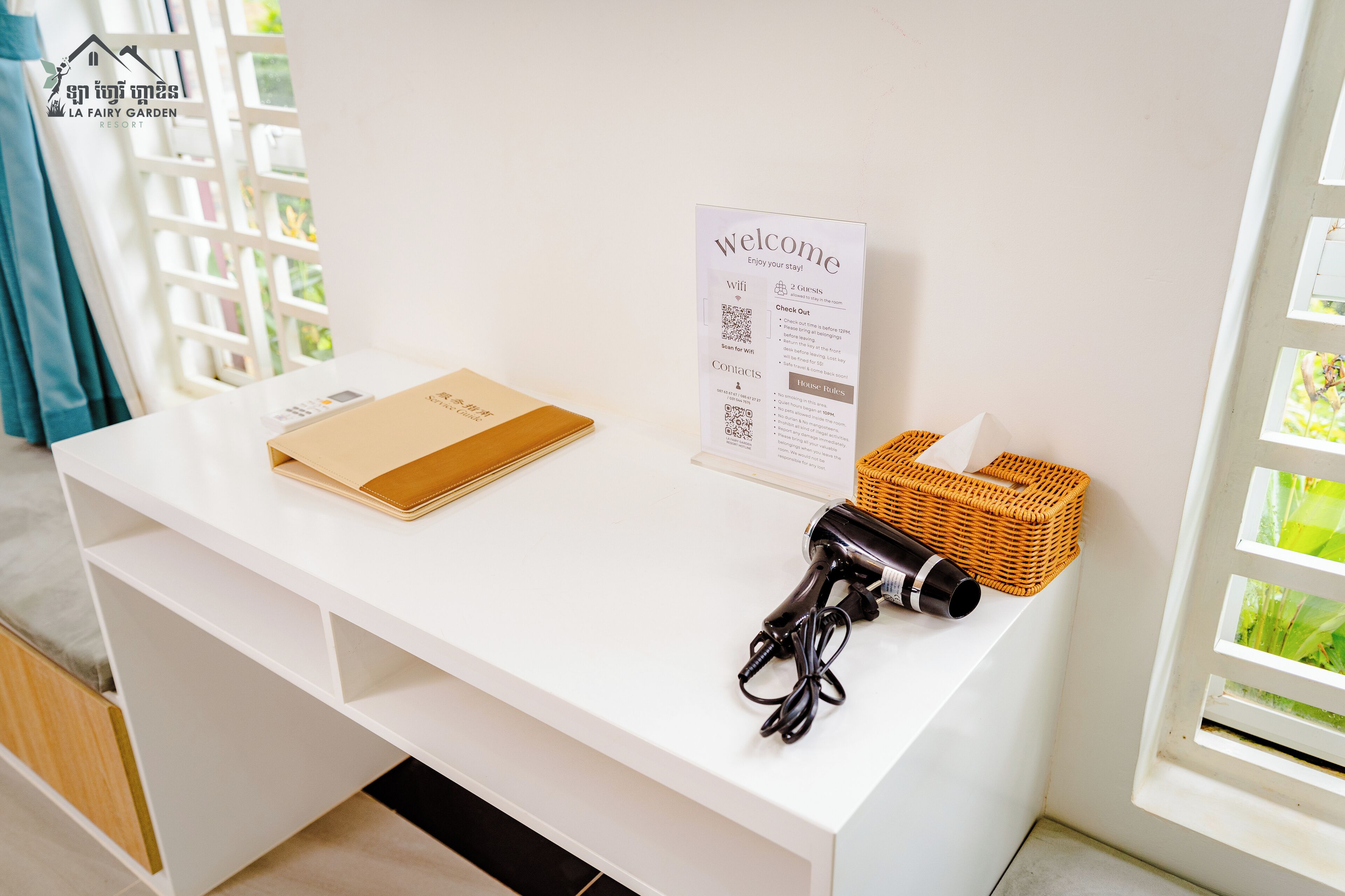 A white reception desk with a welcome sign, a brochure, a hairdryer, and a wicker basket.