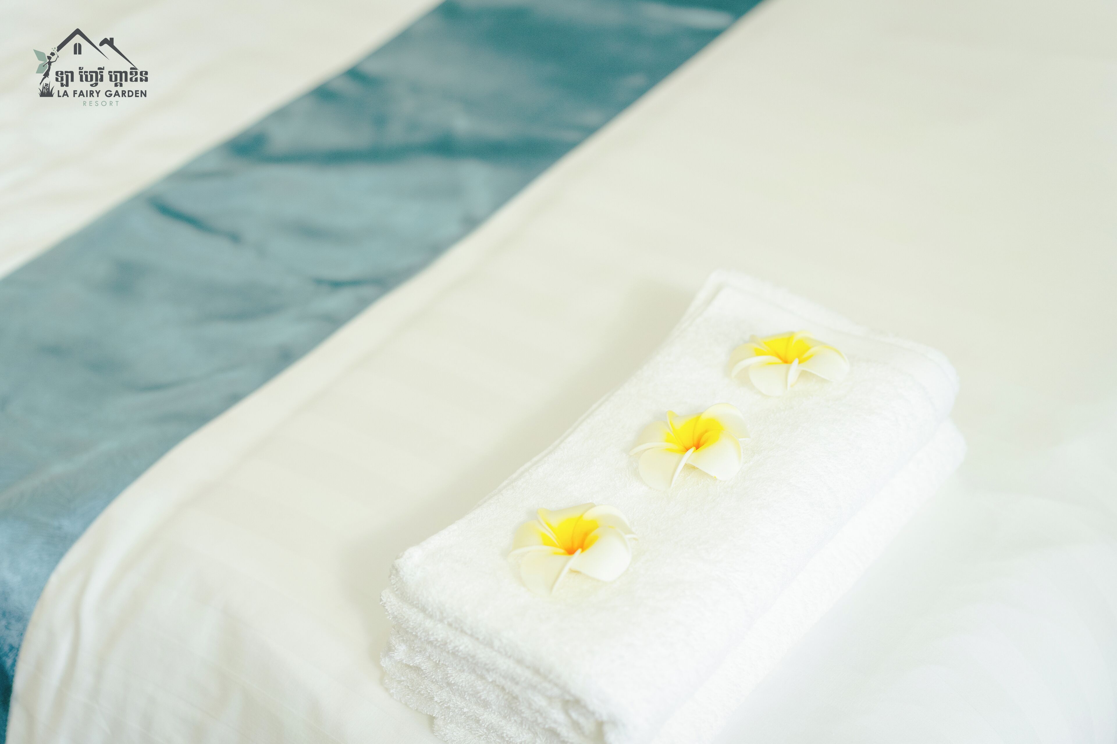 A neatly folded white towel with yellow flowers on a bed with a blue and white striped pillow.