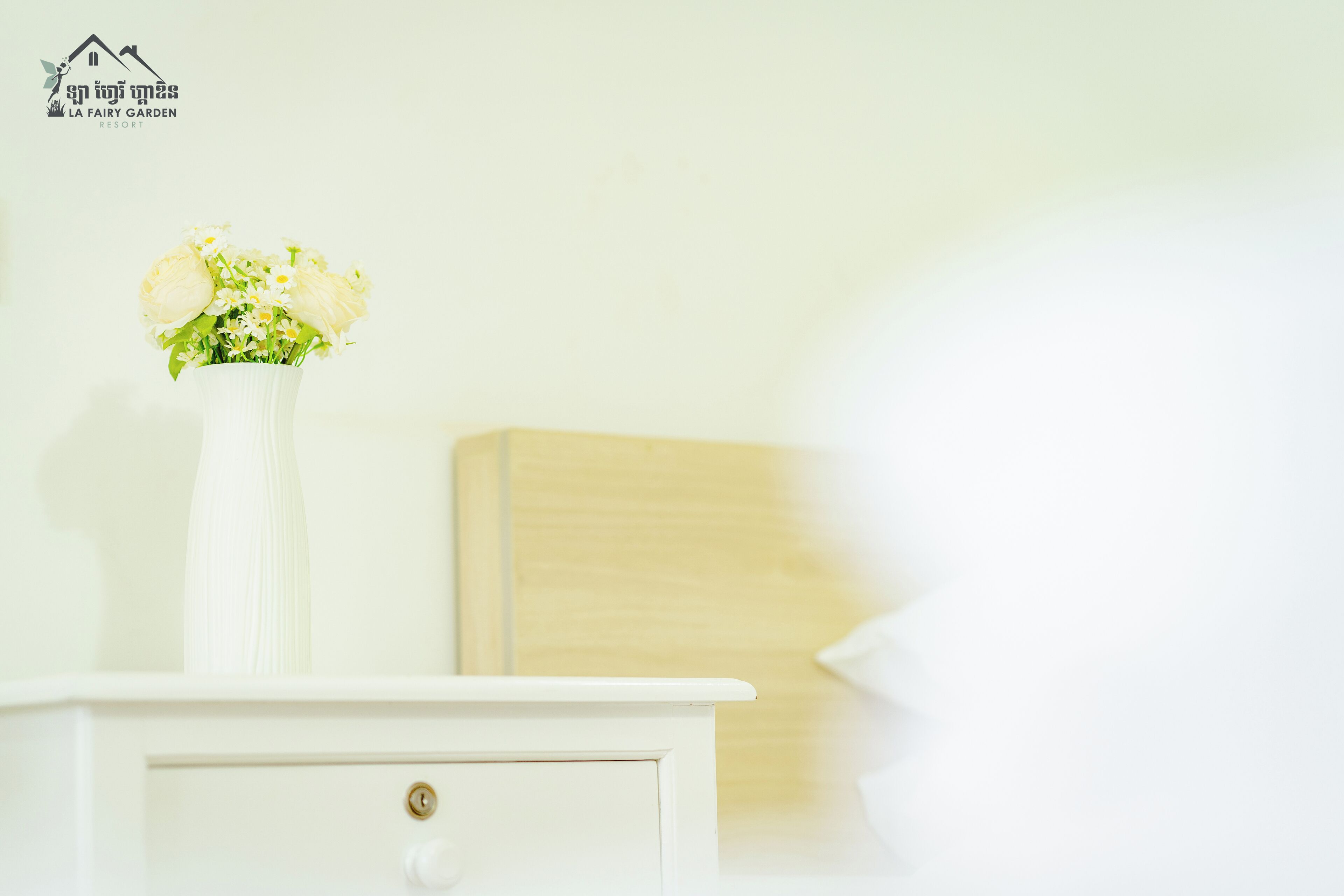 A white bedside table with a vase of flowers, a wooden headboard, and a lock on the drawer.