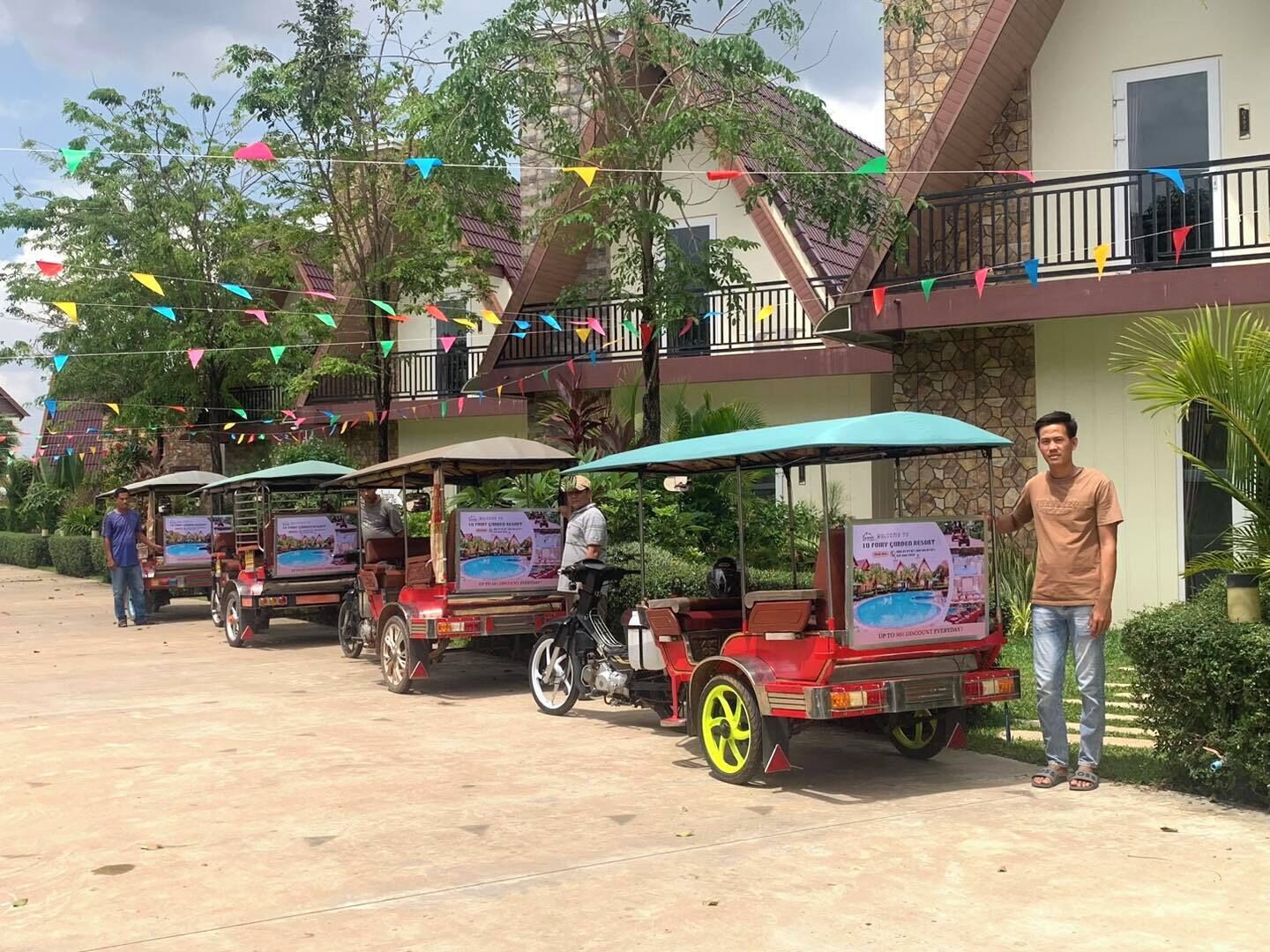 A row of three tuk-tuks parked in front of a building with a balcony, decorated with colorful triangular flags.