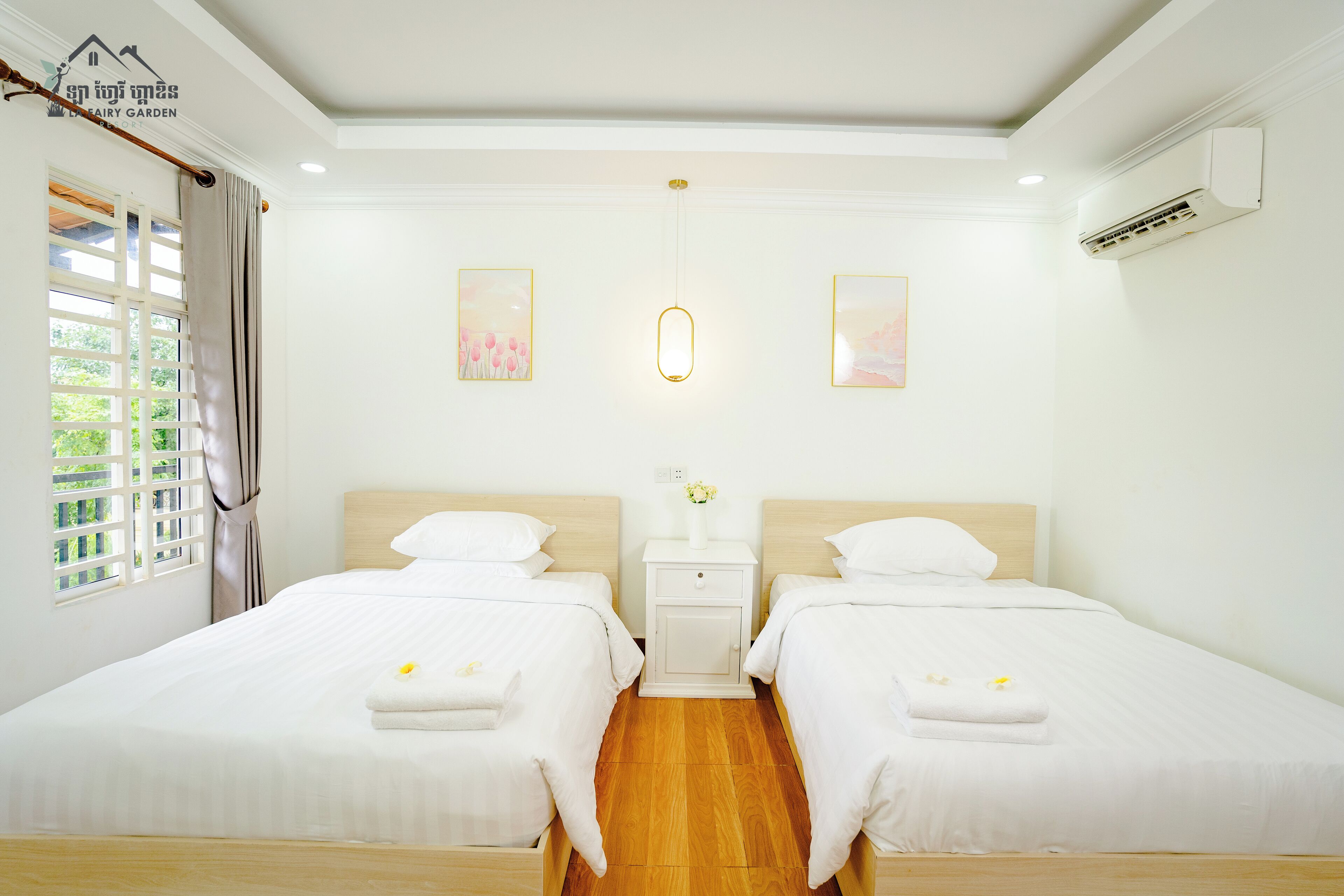 A hotel room with two beds, a nightstand with a vase, and a window with curtains.