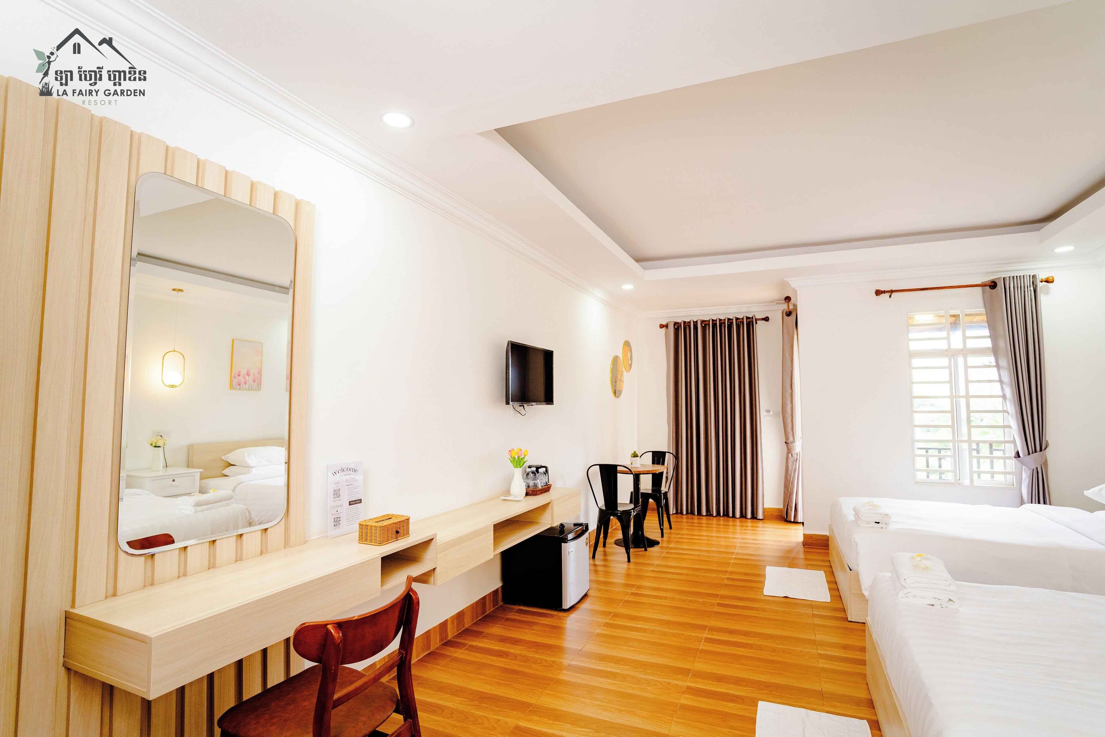 A hotel room with a wooden desk, a chair, a bed, a TV, and a window with curtains.