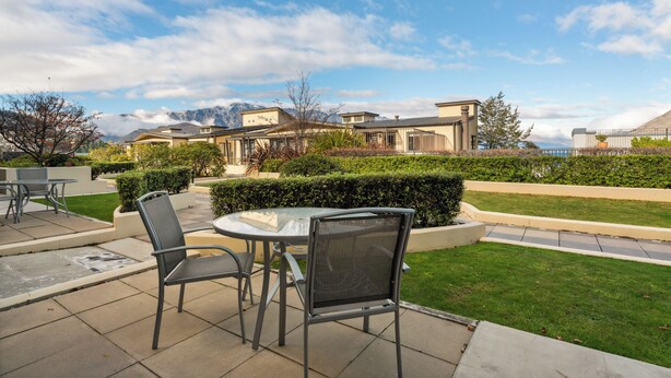 A patio area with a table and chairs, a well-maintained lawn, and a view of mountains in the background. - The Beacon - Town Centre Apartment 620 (Queenstown)