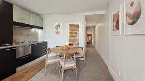 A modern kitchen with dark cabinetry, a stainless steel range, and a dining area with a round table and chairs. - The Beacon - Town Centre Apartment 620 (Queenstown)