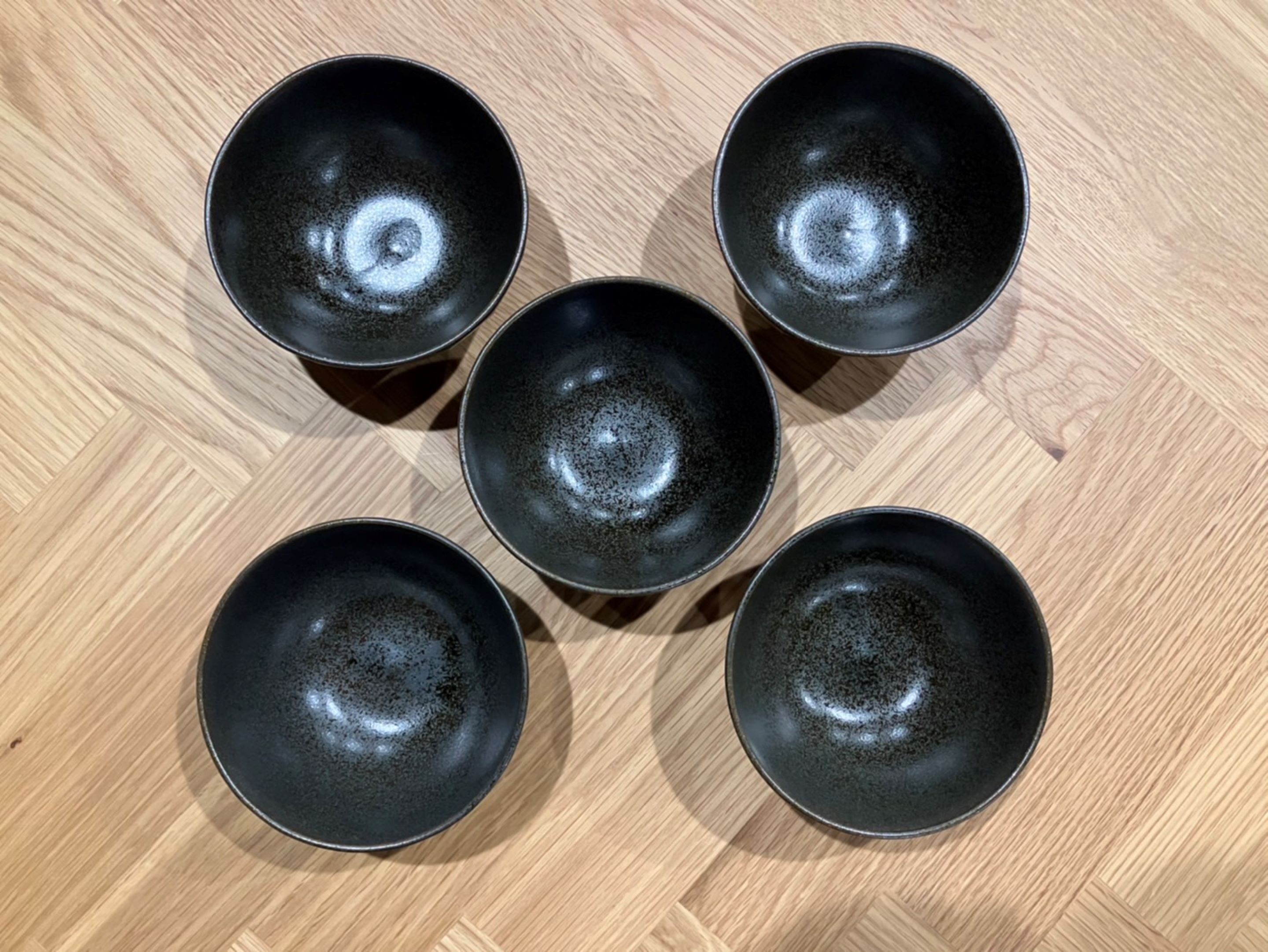 Five black bowls arranged on a wooden floor.