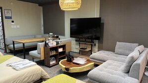 A modern living room with a sofa, a coffee table, a TV, and a dining area. - StayHakata villa  (Fukuoka)