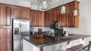 Una cocina con armarios de madera, electrodomésticos de acero inoxidable, encimera de granito e iluminación colgante.
