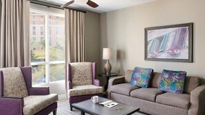 Una habitación de hotel con un ventanal grande, dos sillones, un sofá, una mesa de centro y una lámpara.