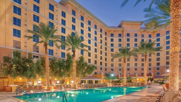Un hotel con una amplia zona de piscina, palmeras y varios balcones.