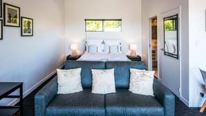 Une chambre d’hôtel moderne avec un grand lit, un canapé gris avec des coussins blancs et une armoire avec un miroir.