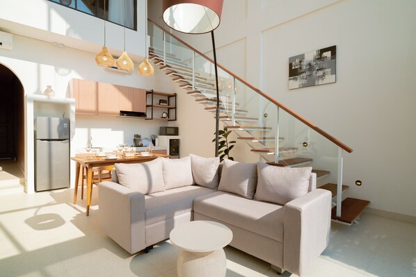 A modern living room with a sectional sofa, a dining area, and a staircase.