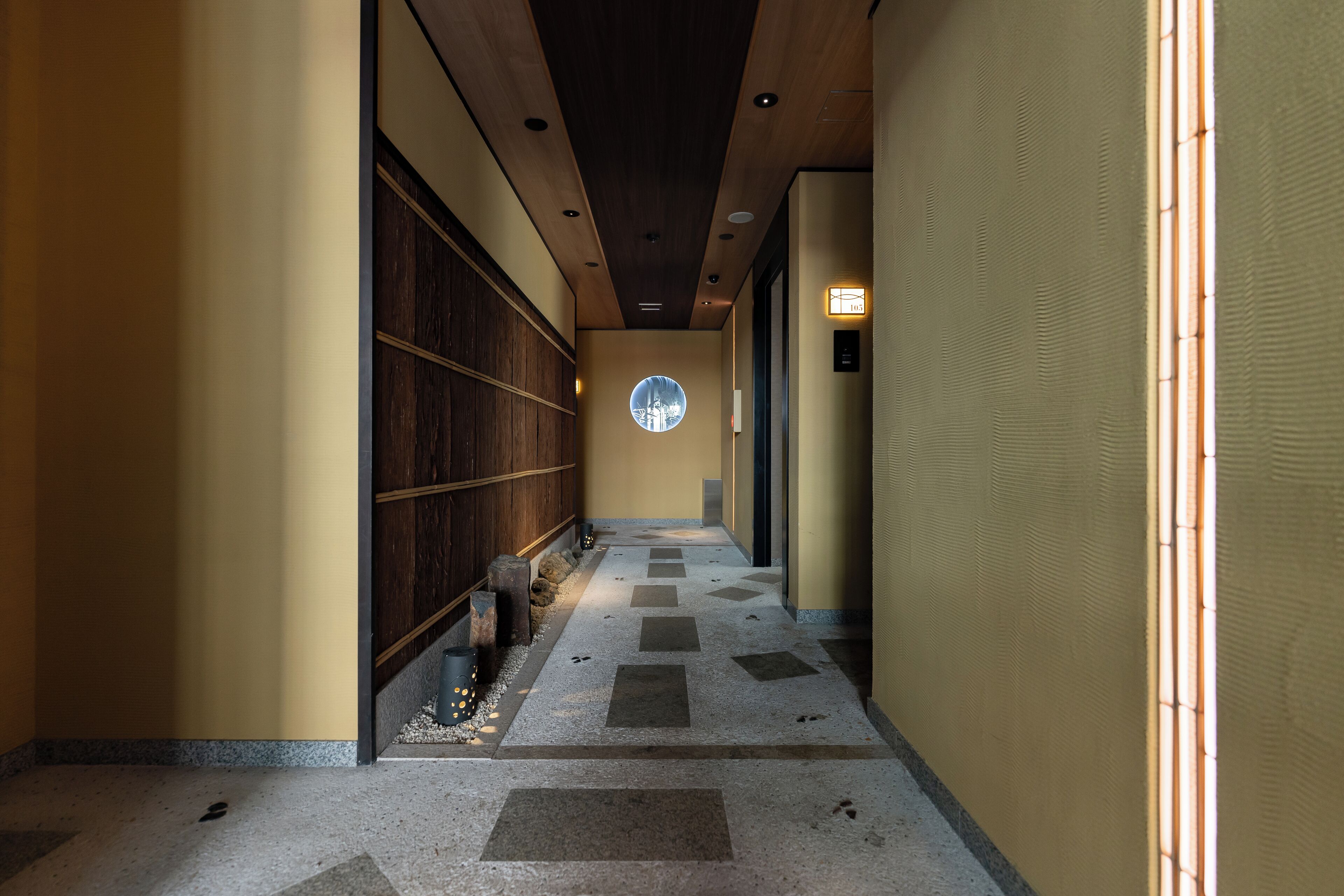 Un pasillo con piso de madera, tragaluz circular y pared de madera.