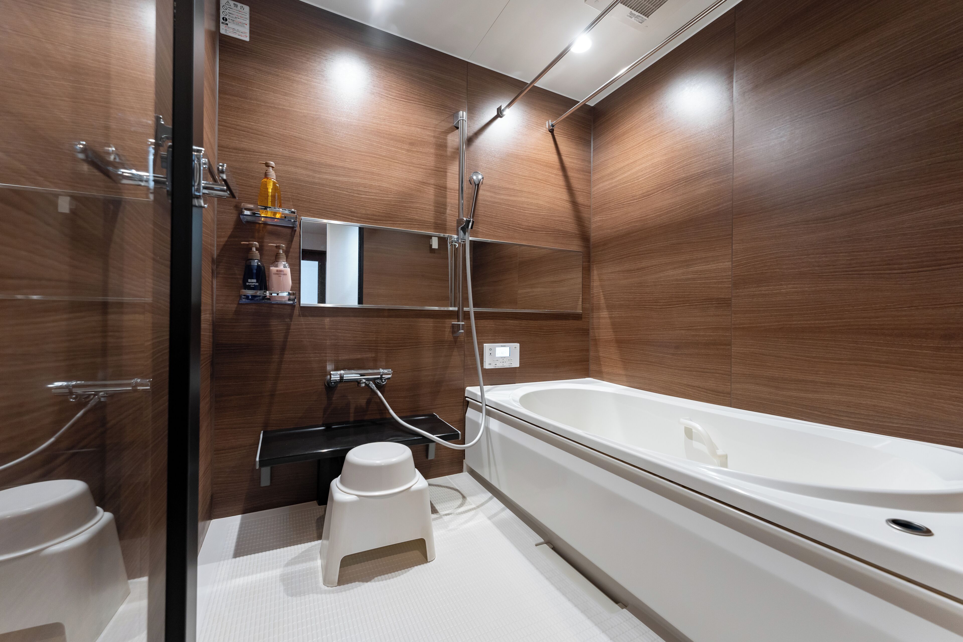 Ein modernes Badezimmer mit einer Badewanne, einer Dusche und einem WC. Es gibt Regale mit Pflegeprodukten und einen Spiegel über dem Waschbecken.