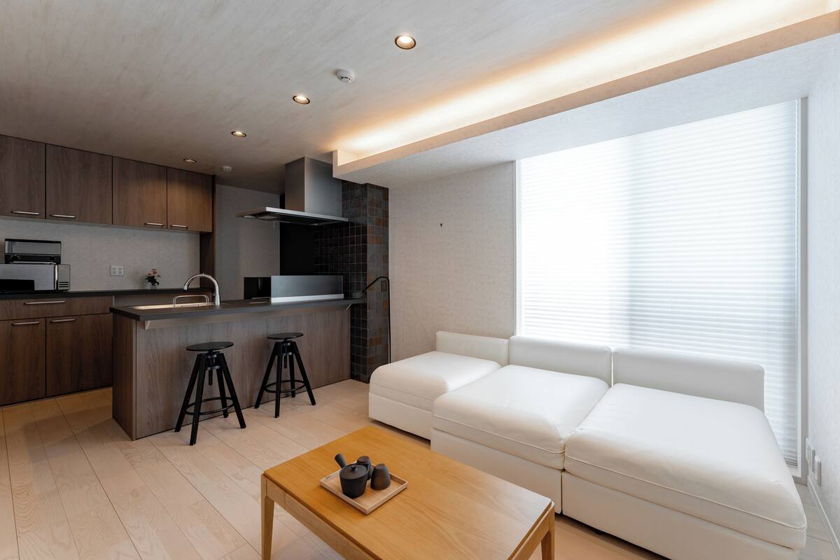 A modern kitchen with a built-in island, bar stools, and a white sofa by a large window.