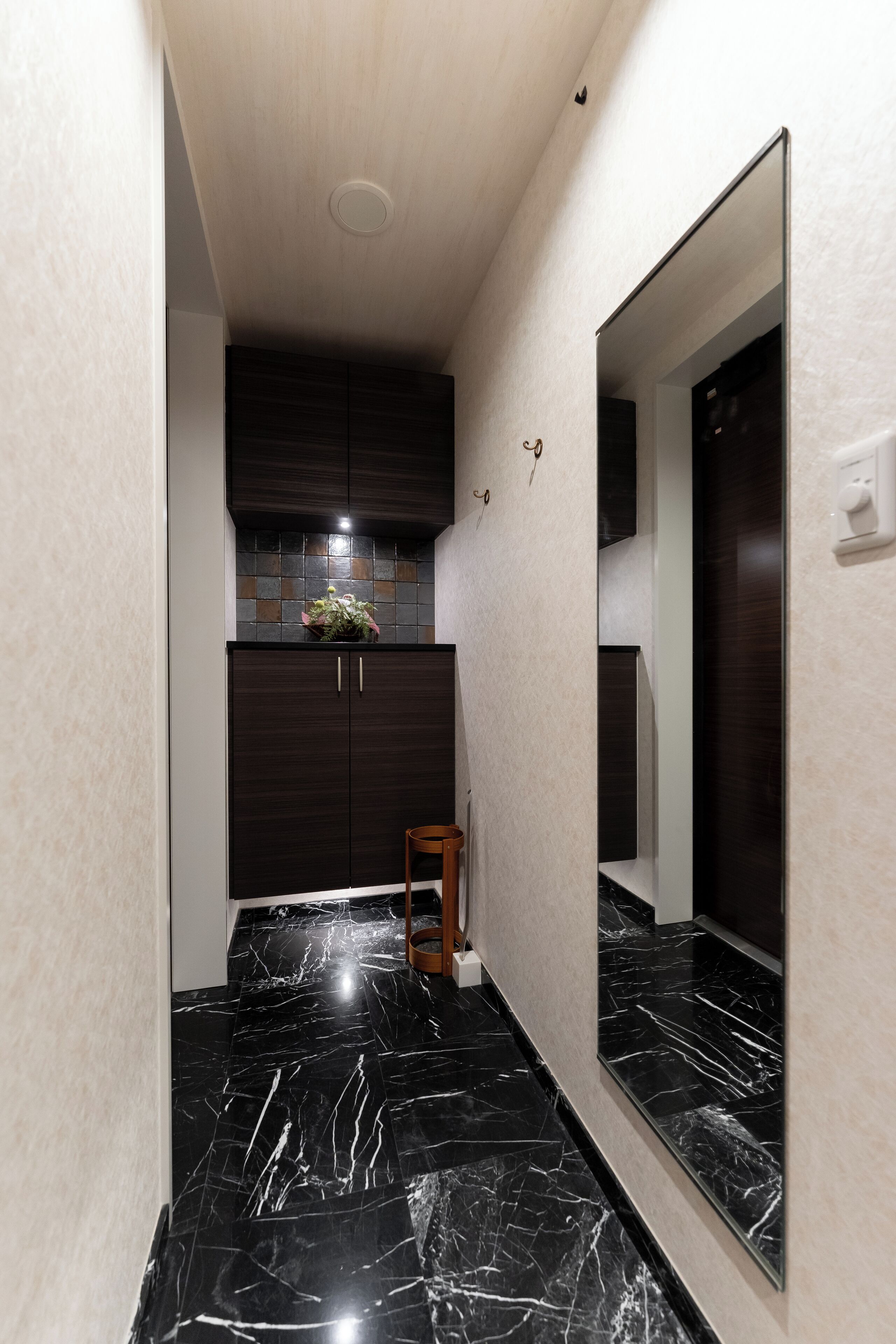 A narrow hallway with a dark wooden cabinet, a potted plant, and a mirror on the wall.