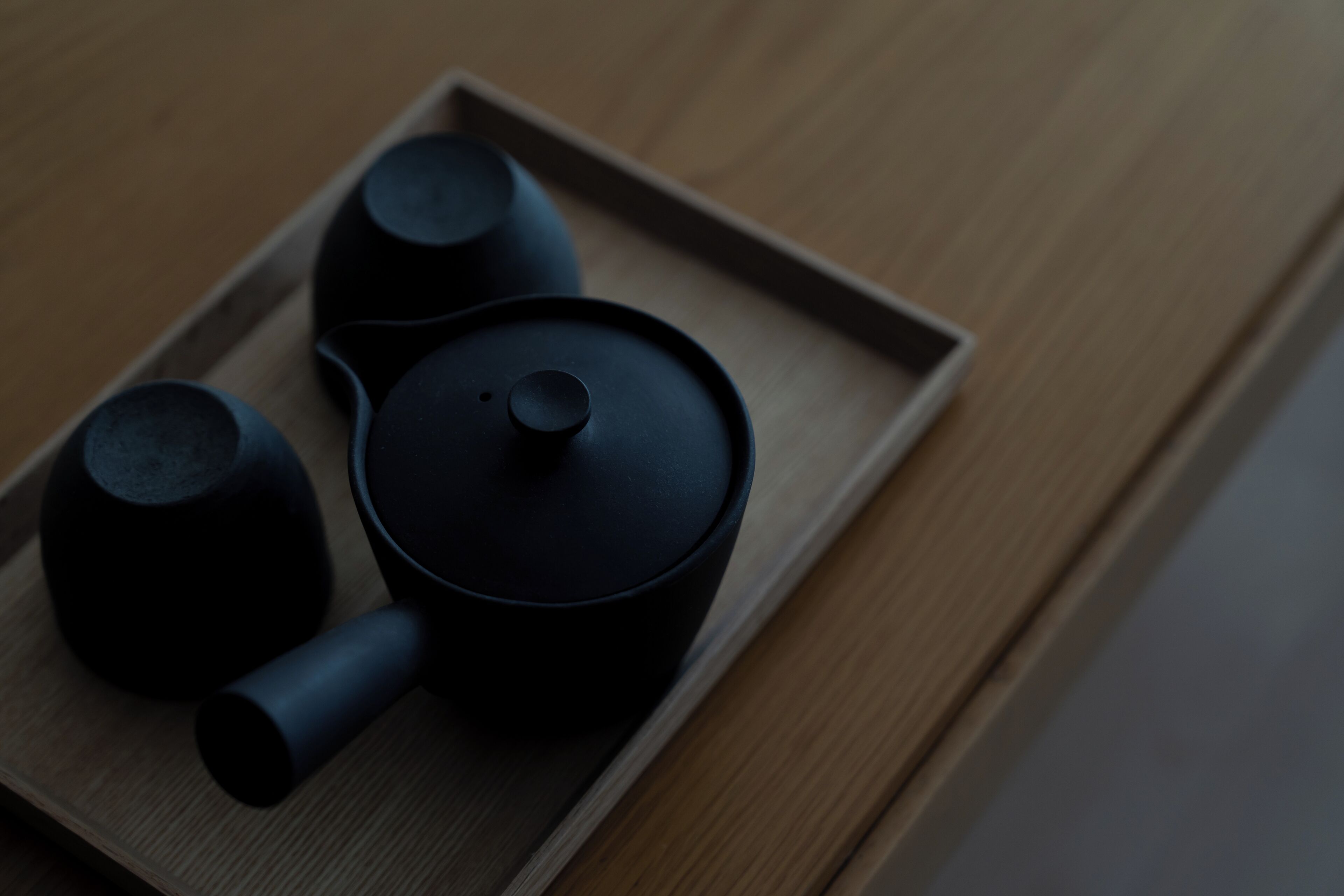 Eine schwarze Teekanne und zwei schwarze Tassen auf einem Holztisch.