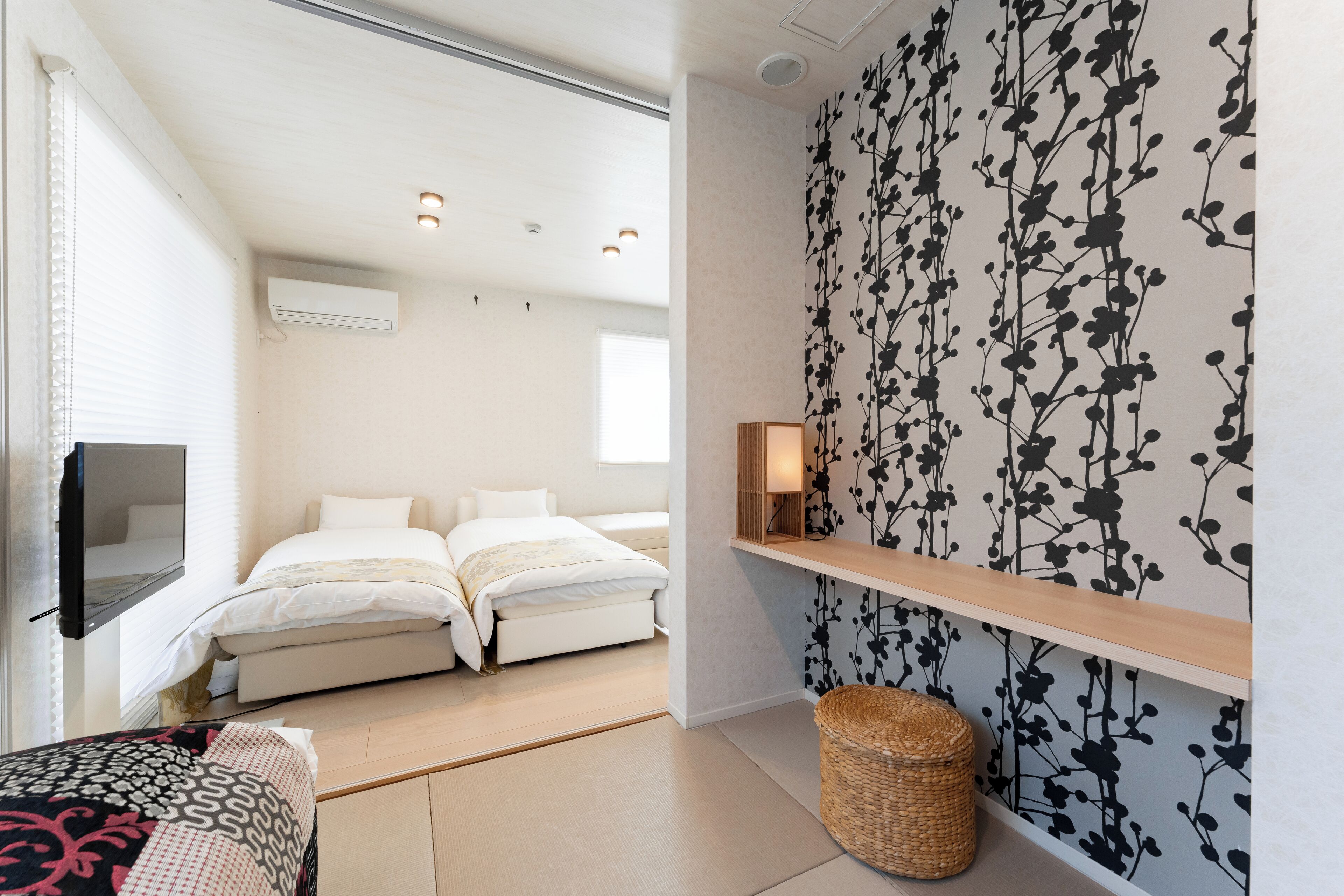 A bedroom with a bed, a TV, a wall-mounted shelf, and a decorative wall pattern.