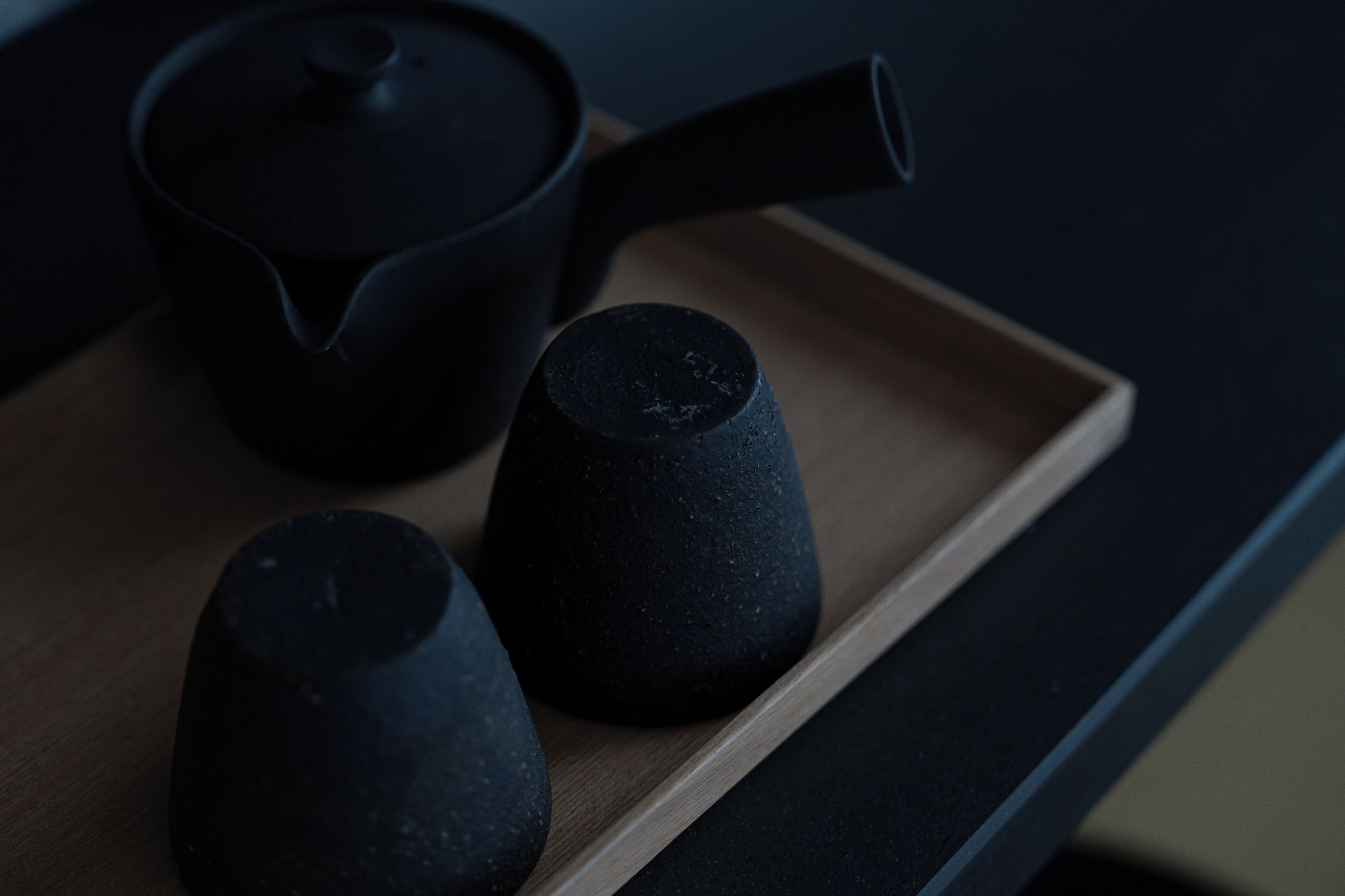 Una tetera negra y dos tazas negras sobre una bandeja de madera.