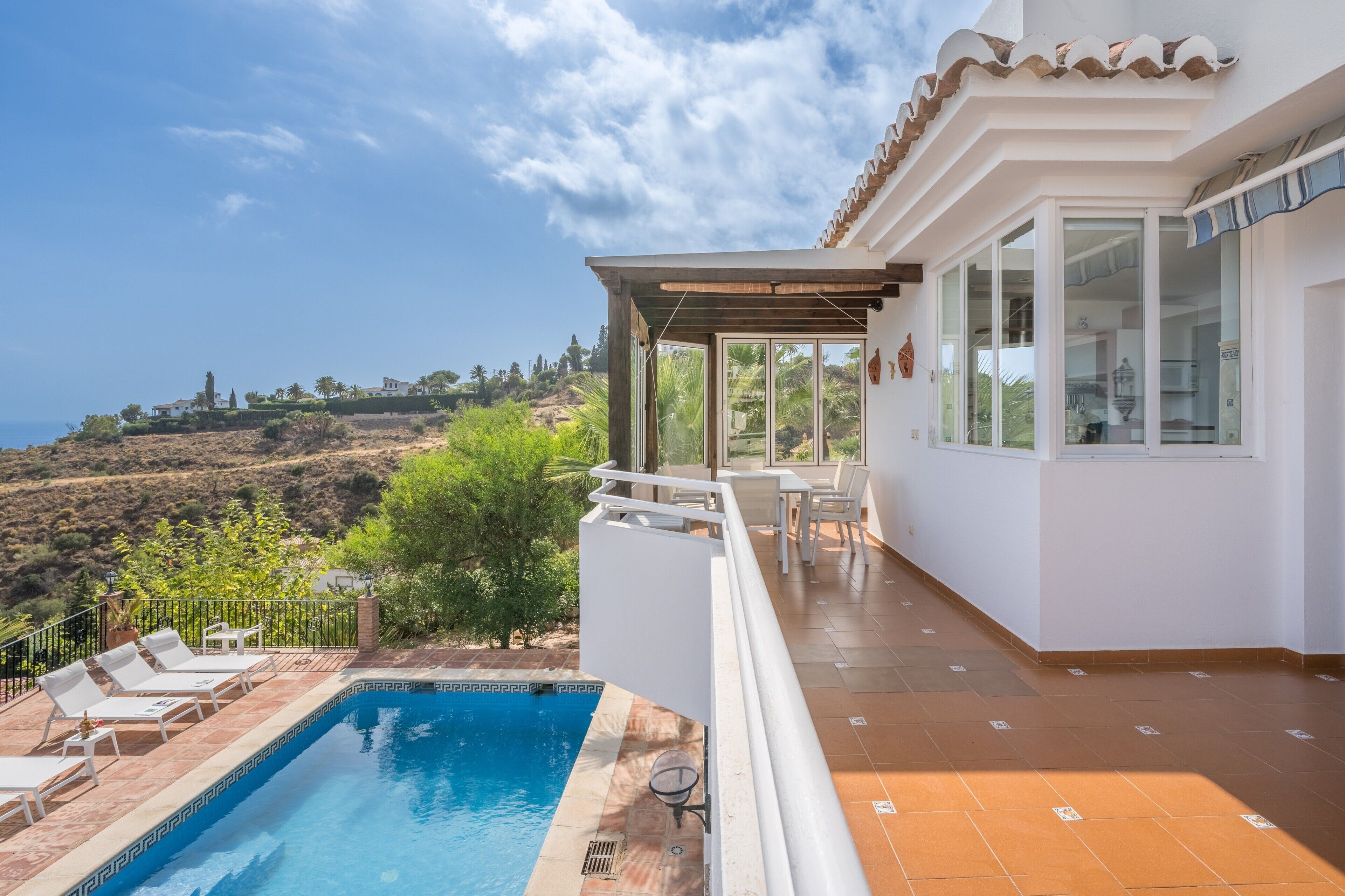 A pool with lounge chairs, a pergola, and a view of a hillside.