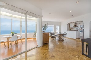 A spacious living area with a sliding glass door leading to a balcony, a dining area with a wooden table and chairs, and a kitchen visible through an archway.