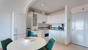 Une cuisine moderne avec des meubles blancs, une table à manger blanche avec des chaises et un four à micro-ondes.