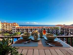 Un balcon avec une table dressée pour le dîner, donnant sur une zone côtière avec des bâtiments et la mer.