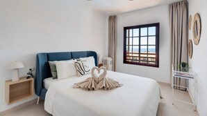 Une chambre d’hôtel avec un lit, un ventilateur de plafond, une fenêtre donnant sur un beau paysage et une table de chevet avec une lampe.
