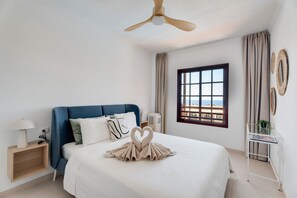 Une chambre d’hôtel avec un lit, un ventilateur de plafond, une fenêtre donnant sur un beau paysage et une table de chevet avec une lampe.