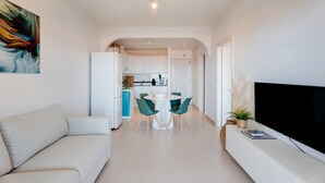 Un salon moderne avec un canapé, un coin repas comprenant une table et des chaises, une cuisine en arrière-plan et un téléviseur posé sur un meuble.