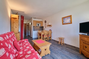 A compact living space with a kitchenette, a dining area, a sofa, a television, and a small table.
