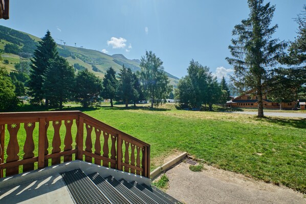 A wooden deck with a metal grate, a grassy area, and a mountain in the background.