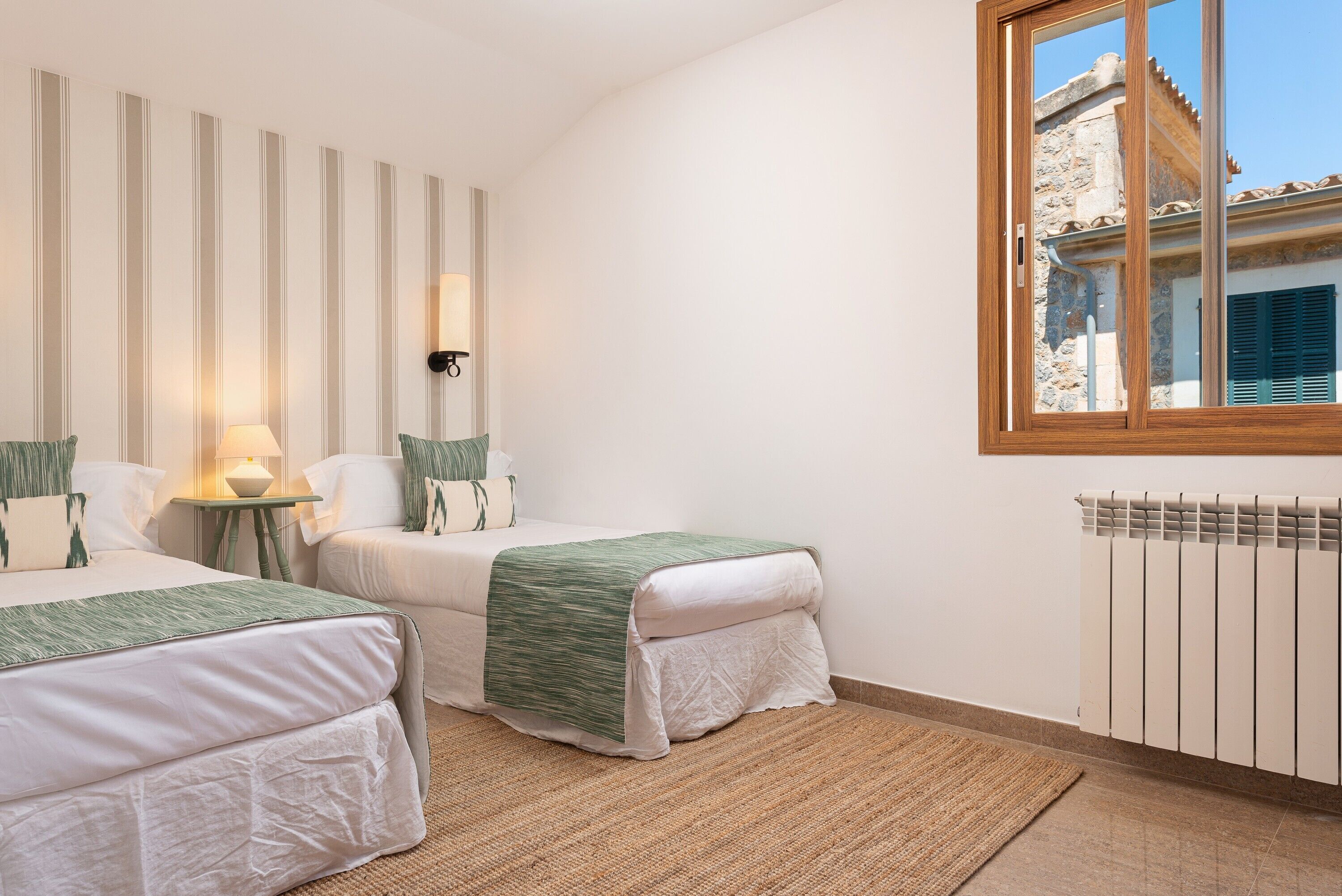 Une chambre avec deux lits, une fenêtre, un radiateur et un mur à rayures verticales.