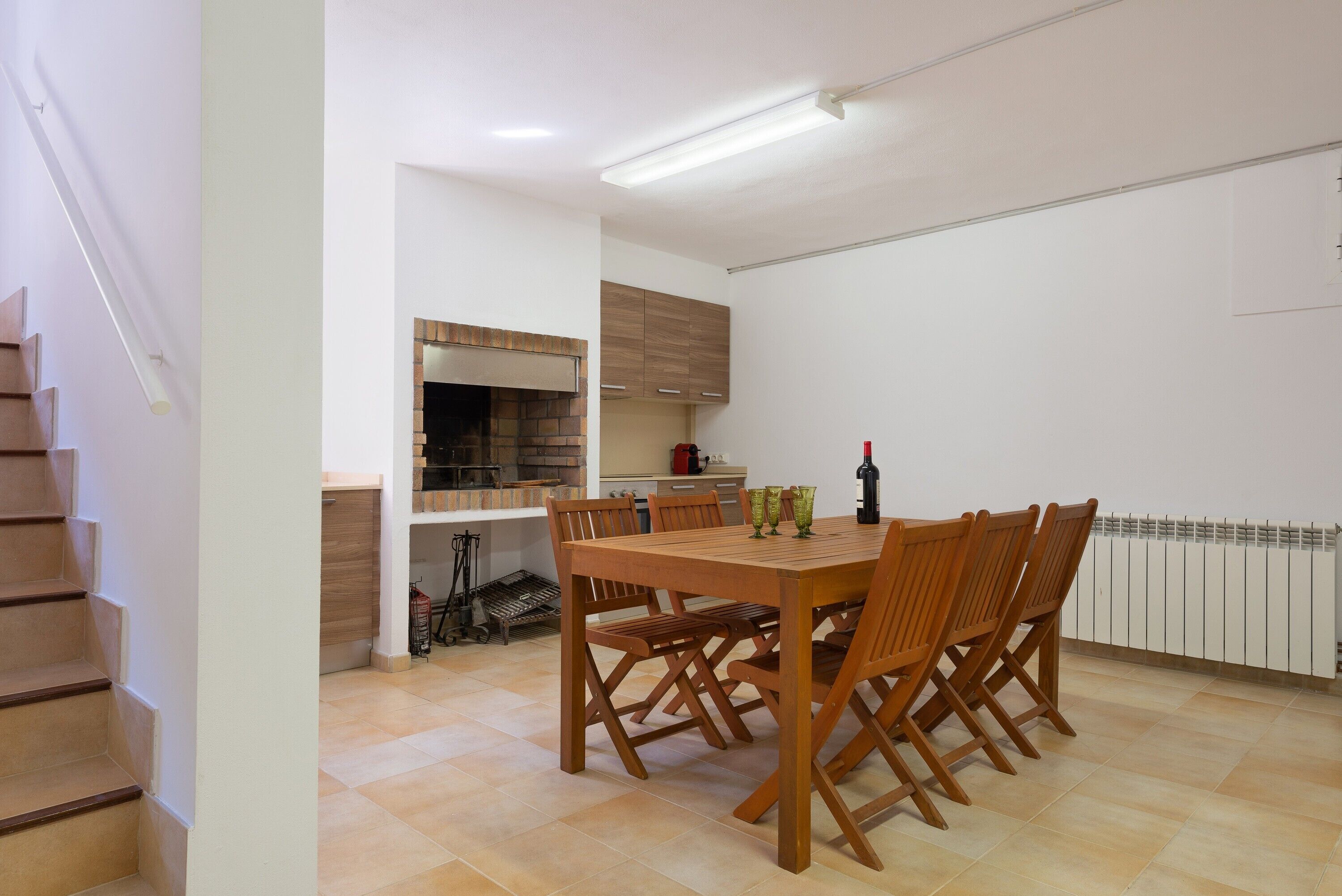 Un coin repas avec une table et des chaises en bois, une cuisine à l’arrière-plan et un escalier sur la gauche.