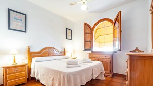 Une chambre bien rangée, avec un lit, des tables de chevet, une commode et une fenêtre avec des rideaux.