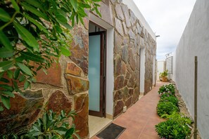 Un bâtiment en pierre doté d’une porte, d’un chemin dallé et d’un petit jardin planté de végétaux.
