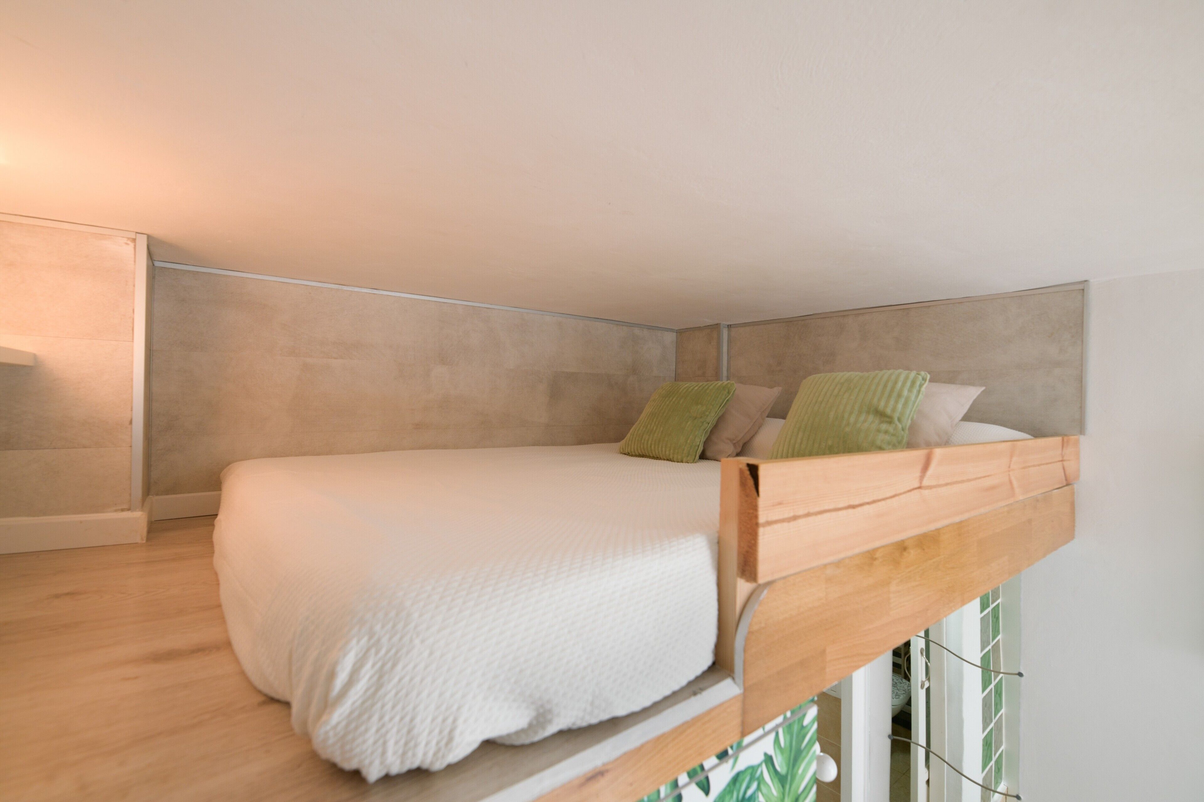 A bunk bed with a wooden frame and white bedding, a small window with a view of greenery, and a light-colored wall.