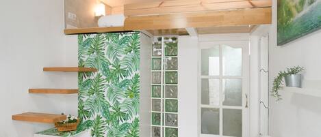 A room with a bunk bed, a white door, a green leaf-patterned wall, and a small shelf with a plant.