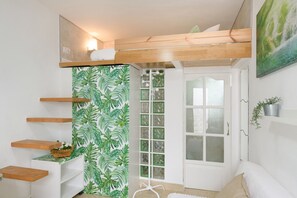 Une chambre avec un lit superposé, une porte blanche, un mur décoré de motifs de feuilles vertes et une petite étagère sur laquelle est posée une plante.