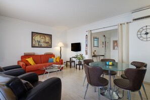 A living room with a red sofa, black leather chairs, a glass dining table, and a flat-screen TV.