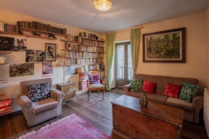 Ein gemütliches Wohnzimmer mit Bücherregal, einer Couch mit gemusterten Kissen, einem Holztisch und einem großen Gemälde an der Wand.