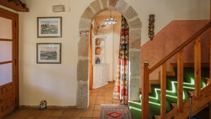 Un passadís amb una porta de fusta, una galeria d'arcs de pedra, una escala amb barana de fusta i una catifa amb dibuixos al terra.
