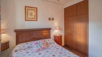 Een slaapkamer met een houten bed, een nachtkastje, een lamp, een kledingkast en een lijst met een afbeelding aan de muur.