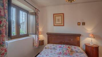 A bedroom with a bed, a window with curtains, a bedside lamp, and a framed picture on the wall.