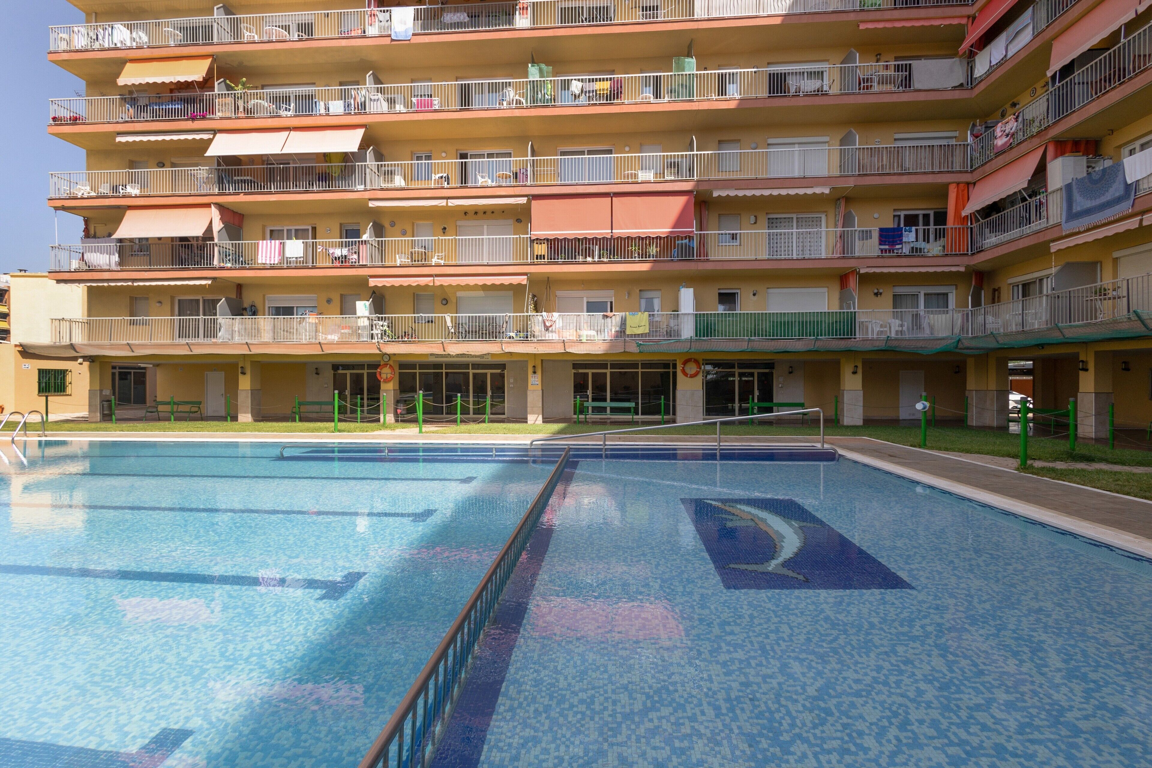 A multi-story residential building with balconies, a swimming pool, and a green lawn.