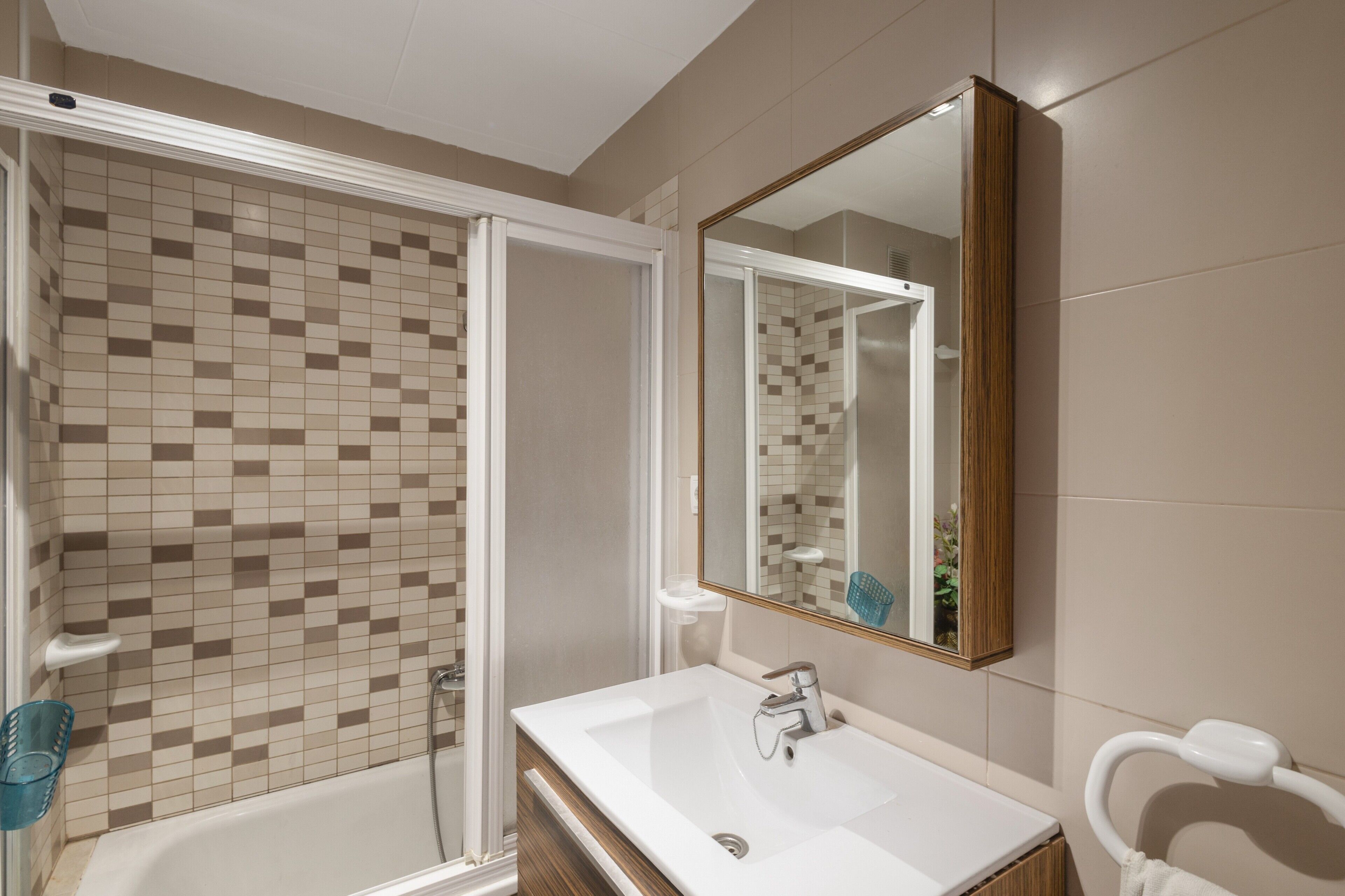 Een badkamer met een douche, een wastafel, een spiegel en een handdoekrek.