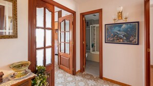 A hallway with a wooden door, a mirror, a framed painting, and a tiled floor.