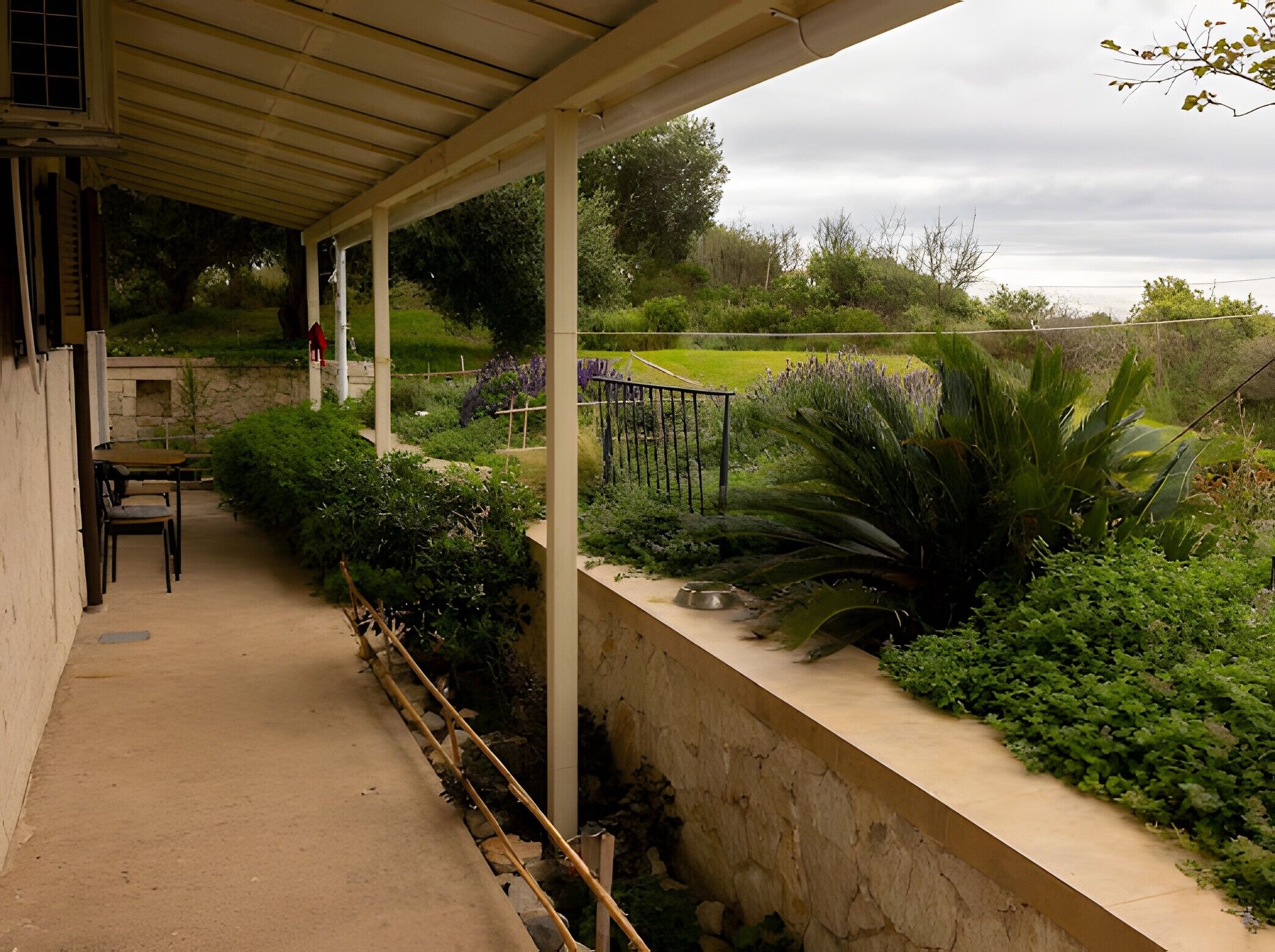 A covered patio with a stone wall, outdoor seating, and a garden with various plants.
